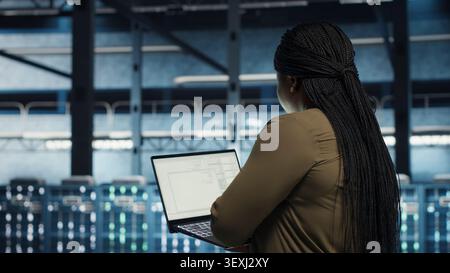 Data center engineer uses a laptop in a server room to upgrade server rigs and increase workload capacity. Stock Photo