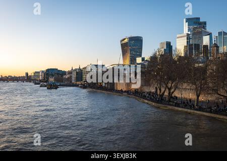 Golden sunset over the River Thames frames London skyline, featuring The Shard and modern riverside offices reflected in the water, with boats, cranes Stock Photo