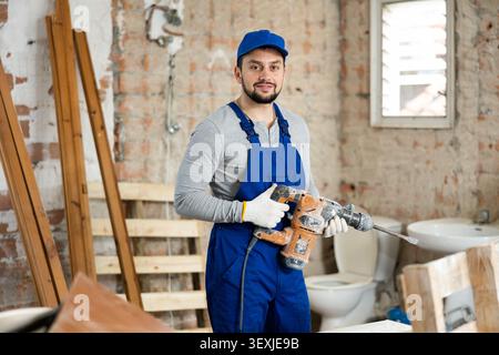Young bearded builder holding pneumatic jackhammer in building under renovation Stock Photo