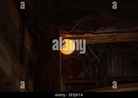 A glowing yellow lantern hangs from rustic wooden beams in darkness, creating warm atmospheric light. Located in Lofoten, this evocative Stock Photo