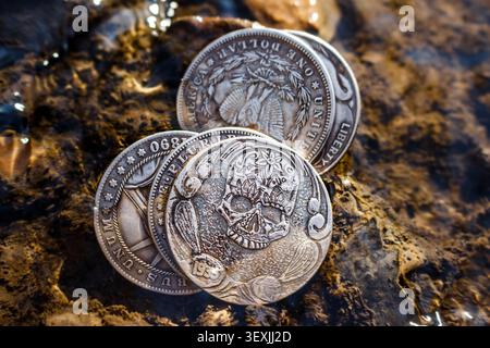 Skull image on old coin lying in stream, souvenir Hobo Nickel coins in shape of Morgan dollar Stock Photo
