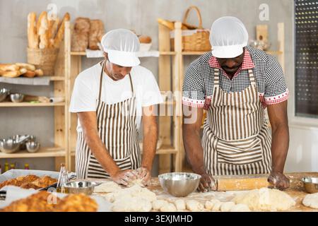 Two bakers working to knead and roll dough in bakery Stock Photo