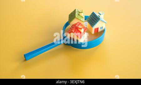 Three colorful miniature model houses with red green and blue roofs sitting inside the rim of a blue magnifying glass on yellow. Stock Photo