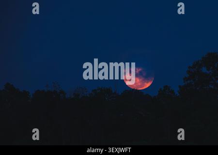 Balikpapan, Indonesia - May 31 2026. A dramatic wide shot of a large, glowing orange-red full moon partially covered by dark clouds. Stock Photo