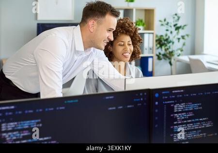 Developers collaborating at computer screens in modern office, coding and mentoring Stock Photo