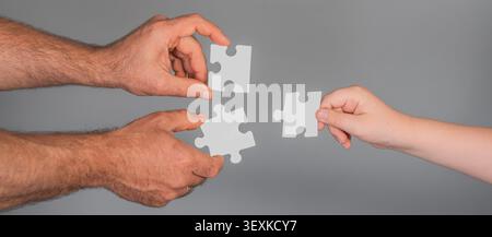 Puzzle pieces create teamwork solution concept. Puzzle assembly shows planning and strategy. Human hands hold puzzle pieces together. Gray background Stock Photo