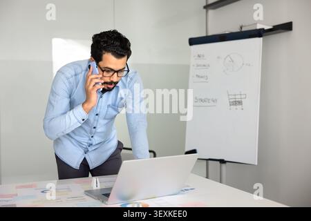 Middle Eastern businessman talking on phone while working on laptop Stock Photo