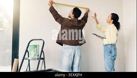 Measuring, tool and couple in new home for renovation, maintenance or property development. Tape, real estate and man with woman for precision on wall Stock Photo