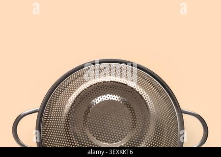 Empty metal kitchen colander on peach background Stock Photo