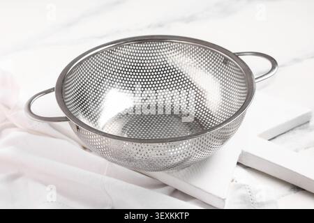 Empty stainless steel kitchen colander on white cloth Stock Photo