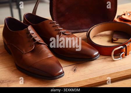Brown leather shoes with belt and bag on wooden table Stock Photo