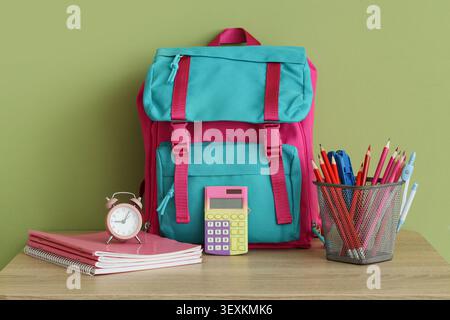 Colorful school backpack with stationery and alarm clock on wooden table Stock Photo