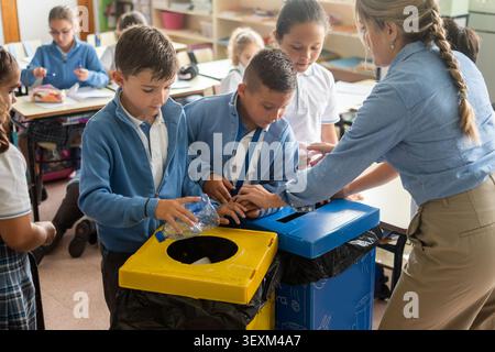 Elementary School Students Learning to Recycle Plastic Bottles with Teacher in Classroom Stock Photo