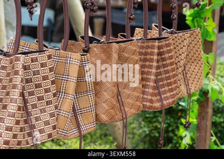 Handwoven natural fiber tote bags with geometric and plaid patterns hanging at a craft market stall Stock Photo