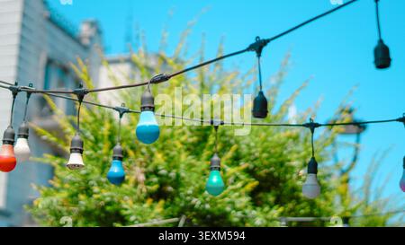 Colorful string lights hanging outdoors against a bright blue sky. Stock Photo