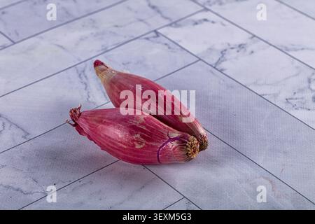 Two red onions with purple skin resting on gray marble tile background. Soft natural lighting highlights texture and color contrast. Minimalist compos Stock Photo