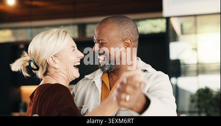 Couple, laugh and holding hands at house for dancing, support and romance for anniversary. Happy, interracial mature people or rhythm in home with Stock Photo