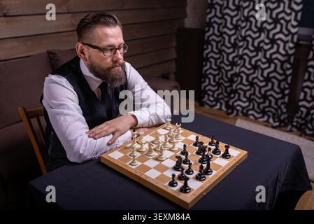 Side view of a concentrated bearded man observing a chessboard setup from above Stock Photo