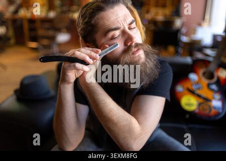 Bearded master leaning back on a leather sofa with a straight razor Stock Photo