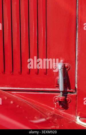 Extreme close-up of a restored classic automobile exterior featuring glossy red paint, a metal hood latch, and vertical cooling louver. The compositio Stock Photo