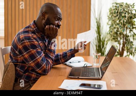 Anxious black man reviewing financial documents and calculating his expenses. Stock Photo