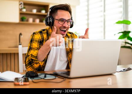 Happy young man is working at home. He is using laptop for online communication. Stock Photo