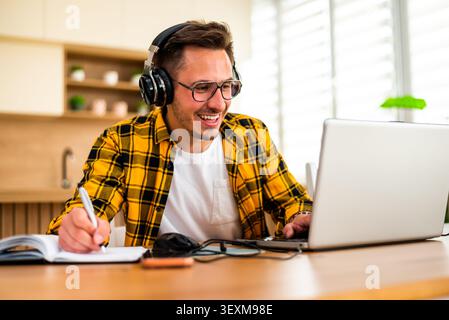 With a cheerful expression, a man uses his laptop, appearing to analyze information or solve a problem online. Stock Photo