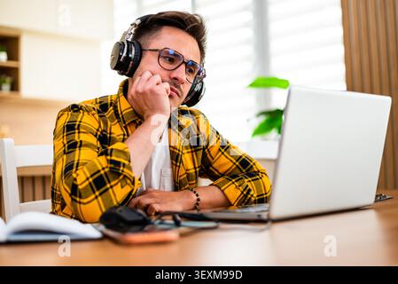 With a pensive and worried expression, a man works on his laptop, appearing to analyze information or solve a problem online. Stock Photo