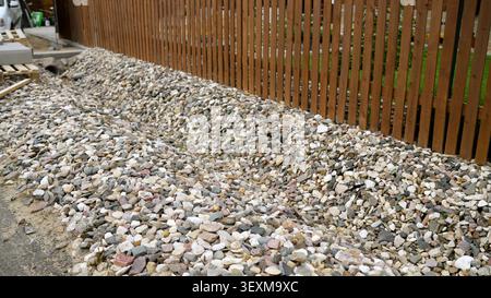 Pile of multicolored gravel beside wooden fence in outdoor construction area Stock Photo
