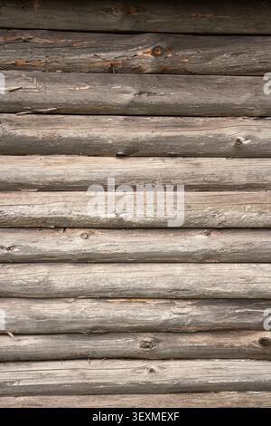 Rows of old, gray-brown wooden logs form a continuous horizontal log cabin wall, showing rough surface texture, cracks, and natural color variations Stock Photo