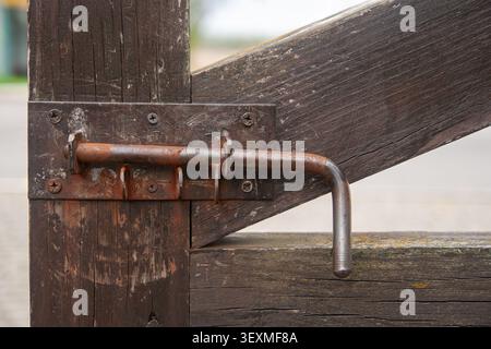 A rusted metal latch (bolt) is focused on a weathered wooden gate, capturing the texture of old wood and metal in an authentic close-up Stock Photo