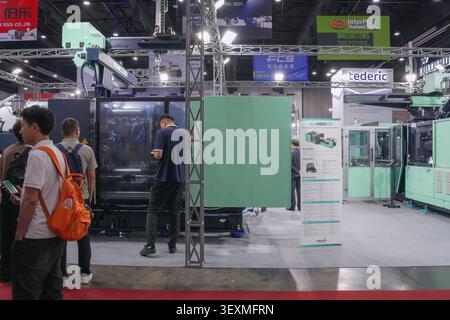 Bangkok, Thailand - June 17, 2026: Businessmen using mobile phones near injection molding machine display at Manufacturing Expo trade show in Bangkok. Stock Photo