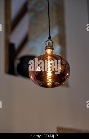 Modern copper glass pendant light bulb glowing. Stock Photo