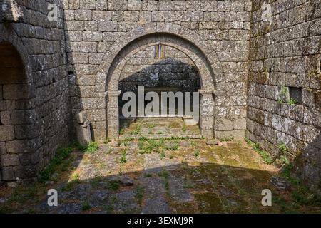 Interior of medieval ruins with a stone arch and altar, covered in moss and vegetation. Stock Photo