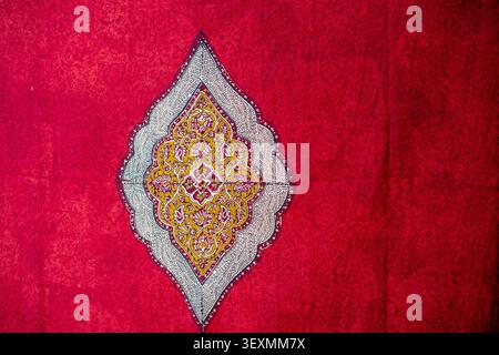 Detail of a traditional red Persian fabric featuring a tone-on-tone damask pattern. In the center stands a large diamond-shaped medallion, finely hand Stock Photo