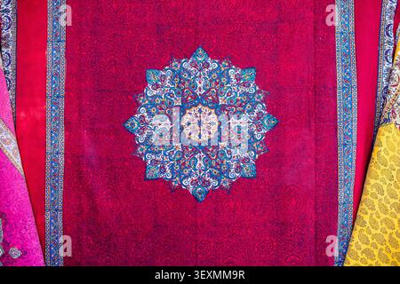 Top view of a luxurious red Persian fabric or carpet enriched with damask floral weaves. The center is dominated by a large star-shaped circular manda Stock Photo