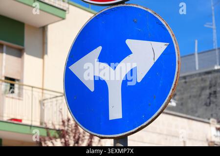 Turn left or right mandatory sign. Road sign in Apulia, Italy. Sign surface deterioration with rusting and peeling paint. Stock Photo