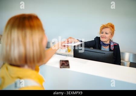 Employee at reception desk assisting customer with checking in and passing documents Stock Photo