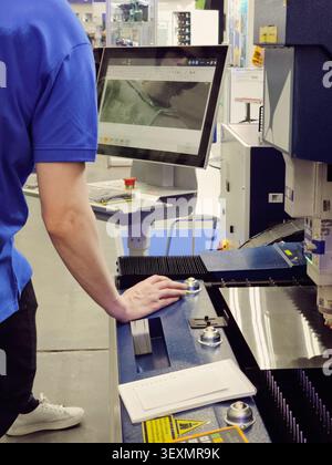 A technician monitors and operates an advanced industrial laser cutting machine via a touch screen interface in a modern manufacturing plant. Stock Photo