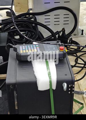 A professional handheld CNC control pendant with a keypad and display screen resting on machine components in a manufacturing workshop environment. Stock Photo