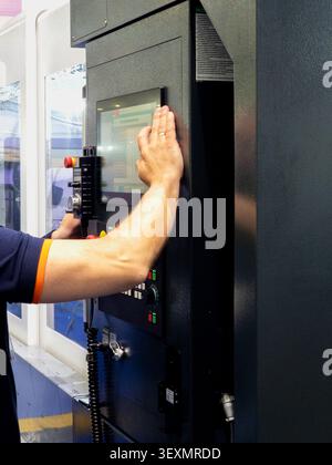 A close-up shot of a technician's hand using a digital touch-screen interface to control and program a professional CNC machine in a modern factory se Stock Photo