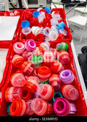 An assortment of vibrant plastic bottle caps and measuring cups in red organizer boxes, showcasing manufacturing components for laundry detergent and Stock Photo