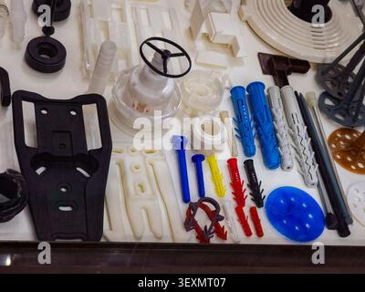 A top-down display showcasing a wide variety of plastic industrial components, including colorful wall plugs, dowels, brackets, and custom molded part Stock Photo