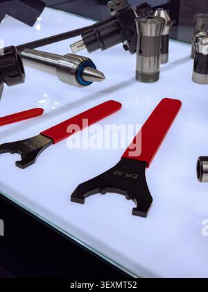 A collection of high-precision CNC machine tooling accessories, including ER32 and ER16 collet wrenches with red handles and metallic live centers, sh Stock Photo