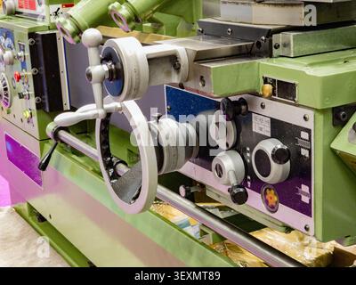 A close-up view of a green industrial metalworking lathe machine, showcasing its precise control handwheels, vernier dials, and knobs used in manufact Stock Photo