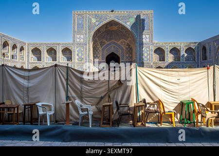 Front view of the courtyard at the Shah Mosque in Isfahan. In the foreground, a beige construction tarp stands with chairs and desks lined up, while t Stock Photo