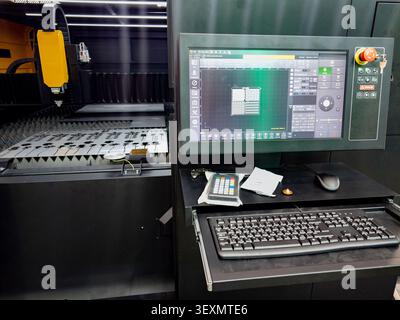Modern CNC fiber laser cutter machine equipped with a digital control system, displaying software layout next to the cutting bed with metal sheets. Stock Photo