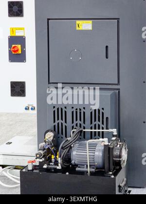 Close-up of a modern industrial hydraulic power pack with an electric motor and pump unit, installed next to a CNC machine cabinet in a manufacturing Stock Photo