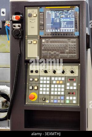 A close-up view of a modern computer numerical control (CNC) machine control panel, featuring a display screen, keyboard interface, adjustment dials, Stock Photo