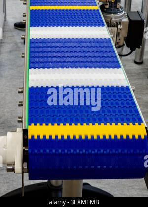 A close-up shot of a modern modular plastic conveyor belt with vibrant blue, yellow, and white segments, designed for efficient automated material han Stock Photo